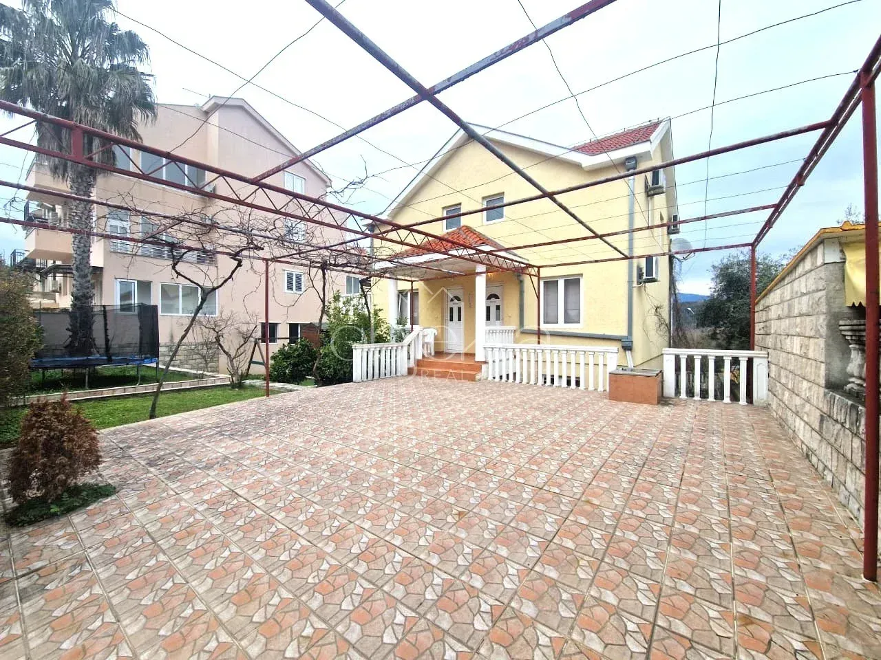 Popločano dvorište sa nadstrešnicom i pogledom na kuću.