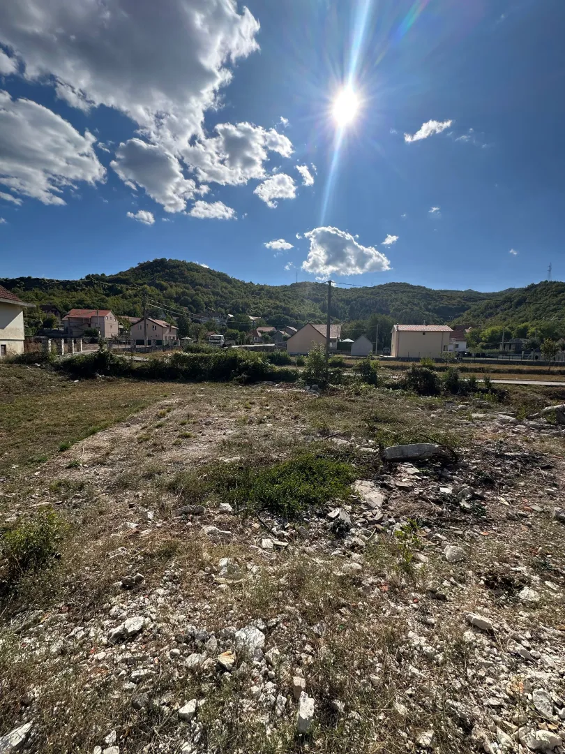 Pogled na plac i okolne kuće sa brdima u pozadini.