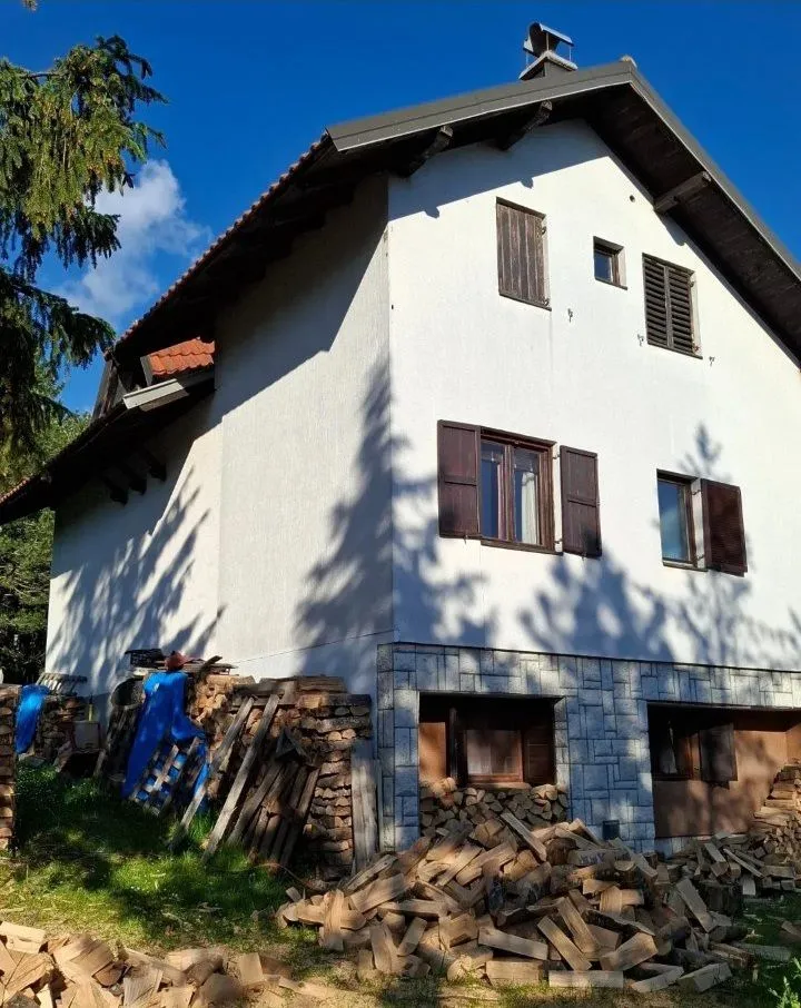 Spoljašnji izgled kuće sa dvorištem i složenim drvima za ogrev.