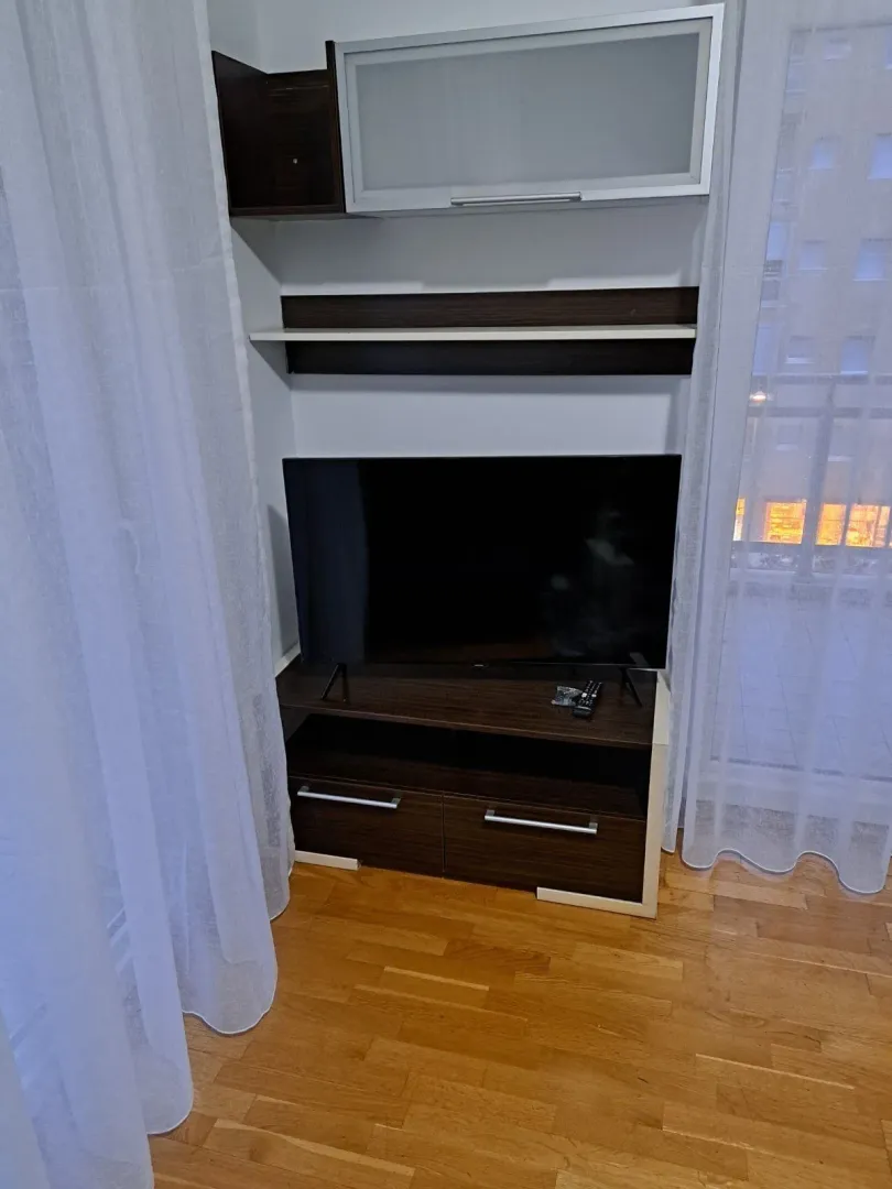 Dnevna soba sa TV policom i komodom pored prozora.