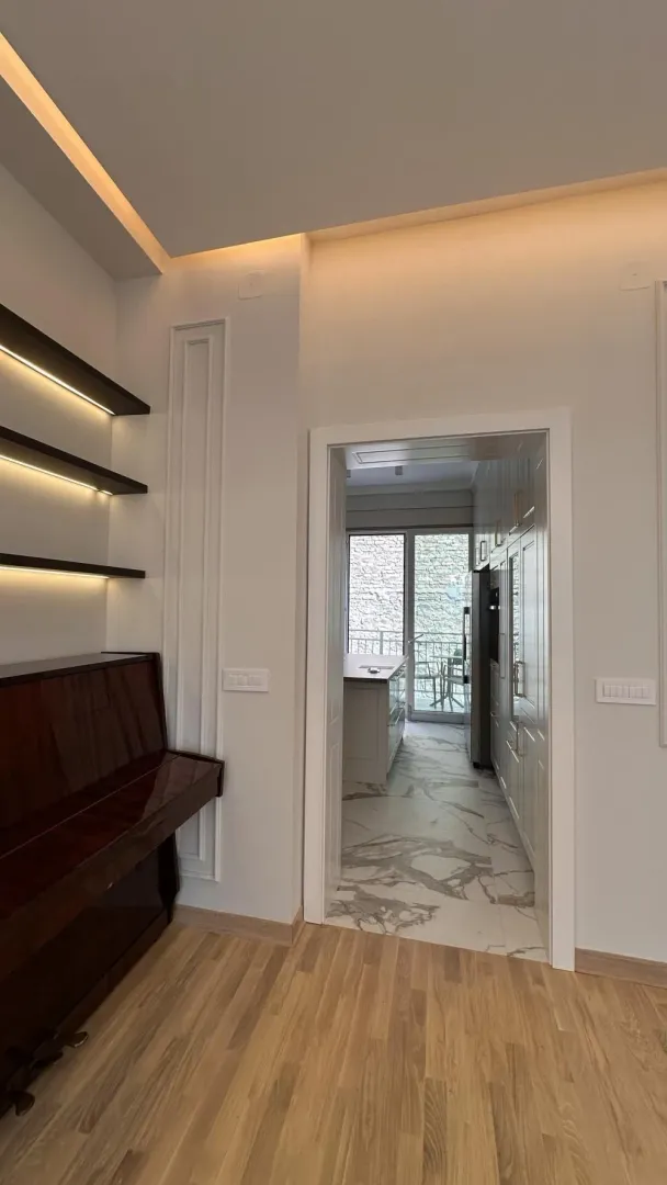View from the living room with a piano and shelves towards the kitchen.