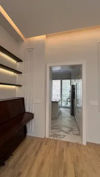 View from the living room with a piano and shelves towards the kitchen. - image 8