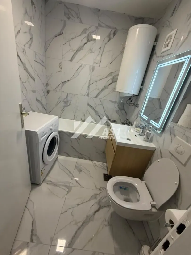 Moderno kupatilo opremljeno tuš kabinom, umivaonikom, WC šoljom i veš mašinom.