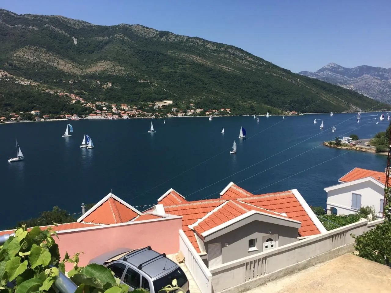 Pogled na zaliv i planine sa terase sa jedrilicama na vodi.
