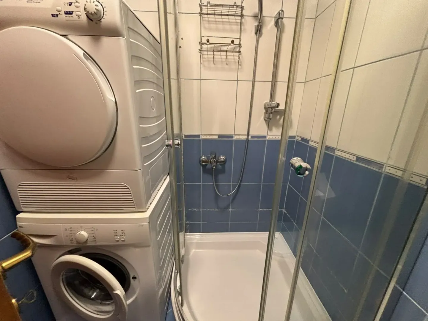 Kupatilo opremljeno tuš kabinom i mašinama za pranje i sušenje veša.