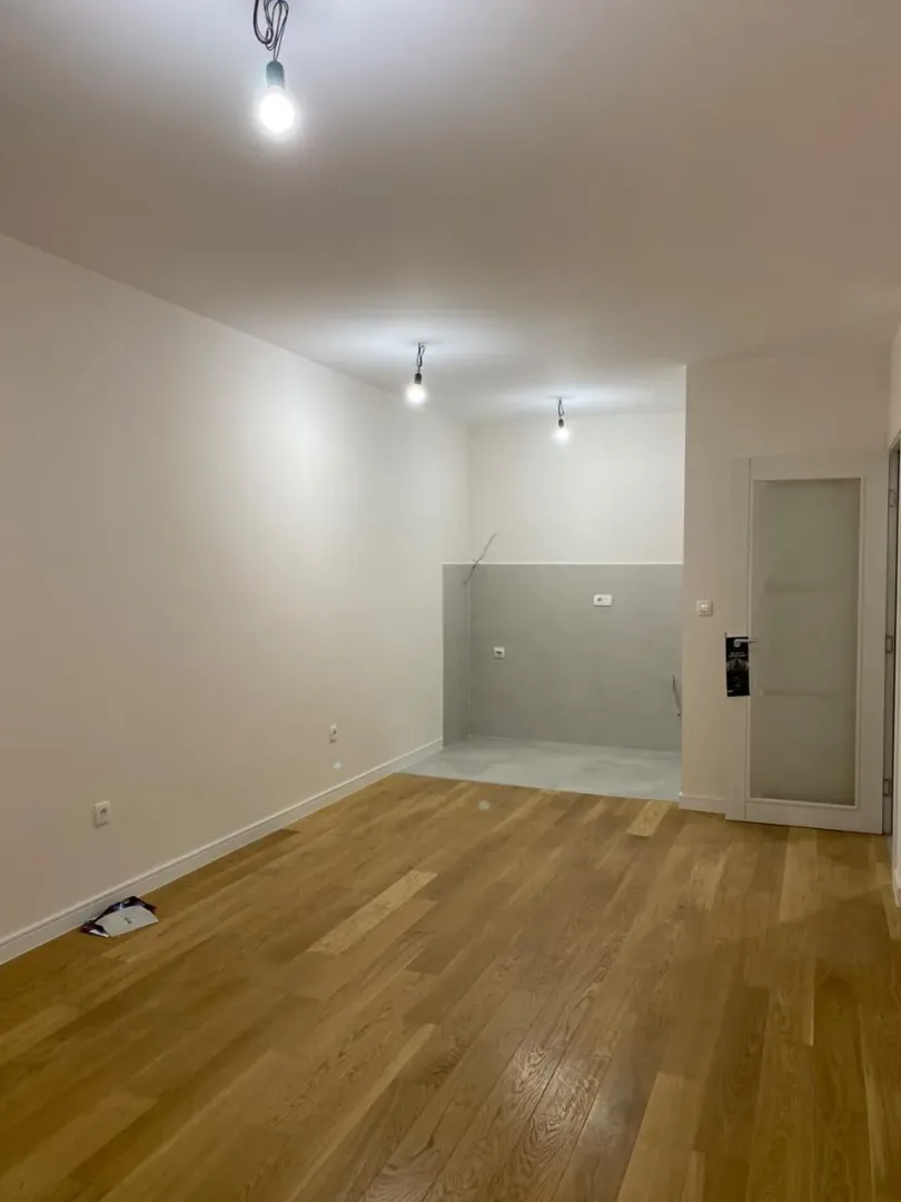 Empty room with wooden flooring and a prepared kitchen area.