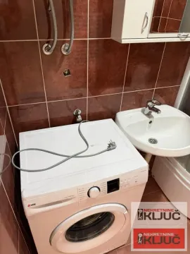 Kupatilo sa veš mašinom, umivaonikom i braon zidnim pločicama. - image 13