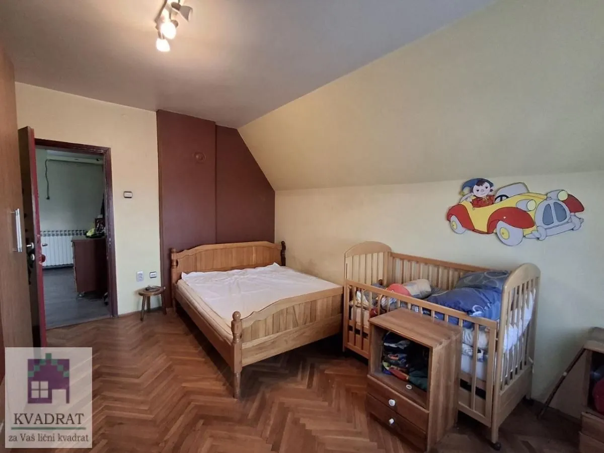 Spavaća soba sa drvenim krevetom i dečjim kreveca pod kosim krovom.