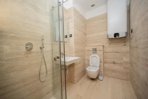 Bathroom lined with beige tiles featuring a shower cabin, washbasin, and toilet. - image 4