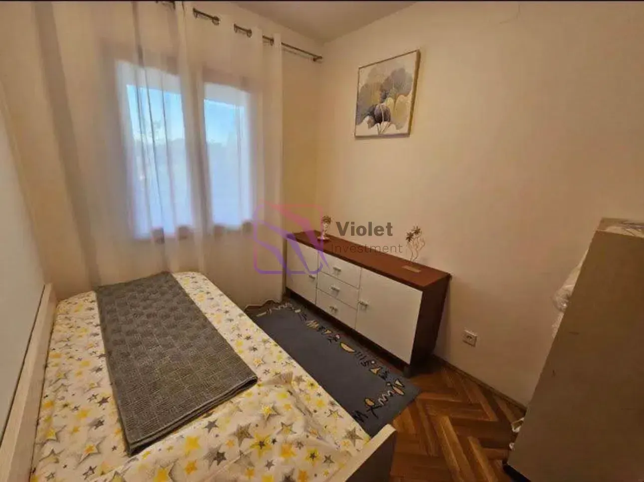 Manja spavaća soba sa krevetom, komodom i prozorom sa zavjesama.