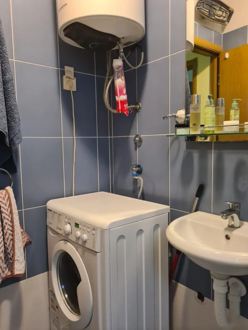 Manje kupatilo sa plavim zidnim pločicama, umivaonikom i veš mašinom.
