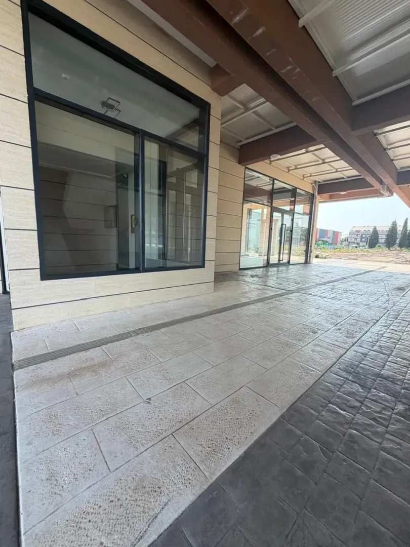 View of the exterior part of the commercial space with a tiled walkway and large glass shopfronts.