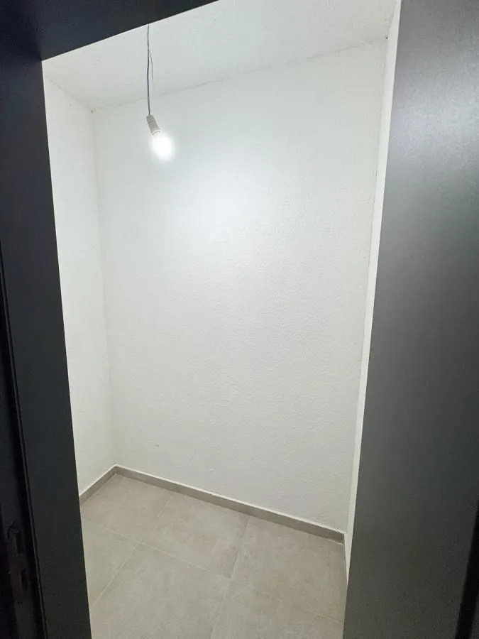 Prazna prostorija sa bijelim zidovima i sijalicom.