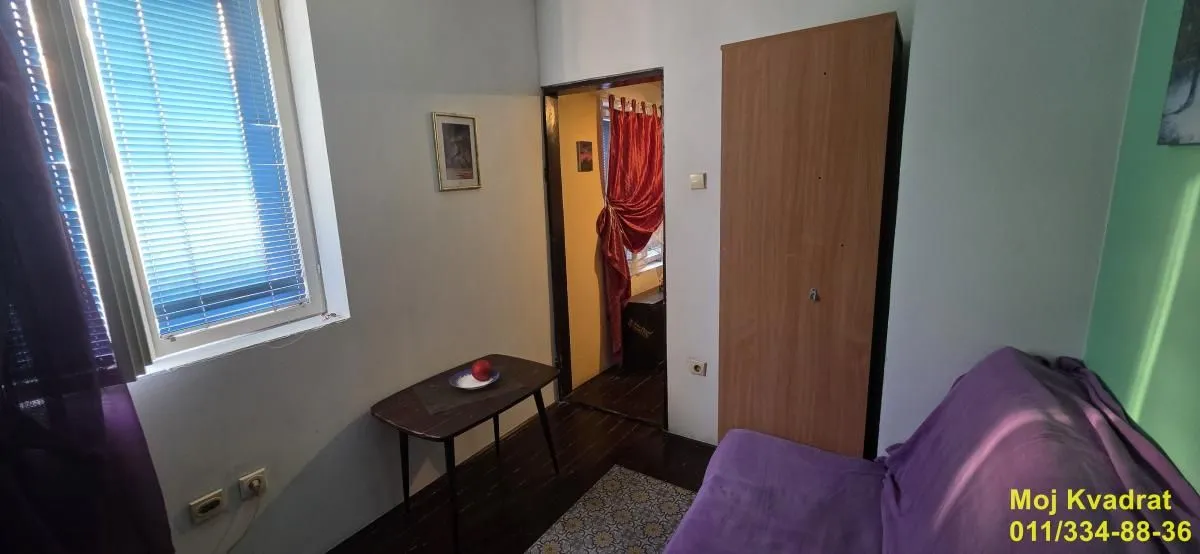 Dnevna soba sa kaučem, malim stolom i prozorom sa žaluzinama.