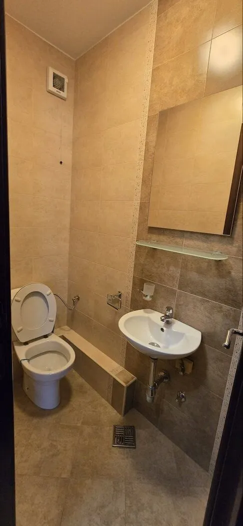 Smaller bathroom tiled with ceramic tiles featuring a toilet and a sink.