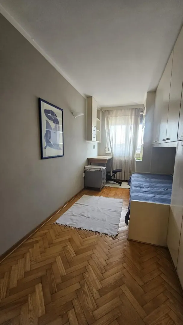 Manja spavaća soba sa krevetom, ugradnim ormarima, radnim stolom i parketom.