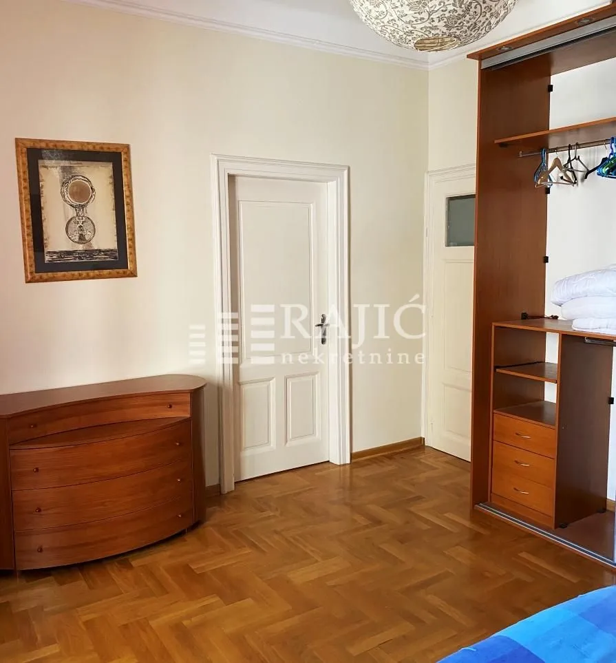 Bedroom with a wooden wardrobe, chest of drawers, and parquet flooring.