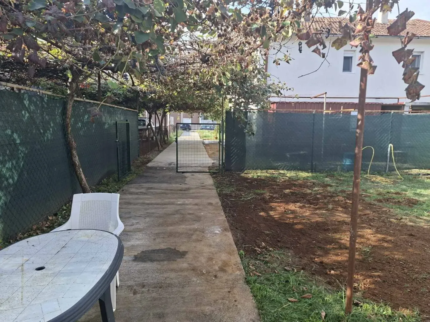 A backyard with a paved pathway, greenery, and an outdoor table.