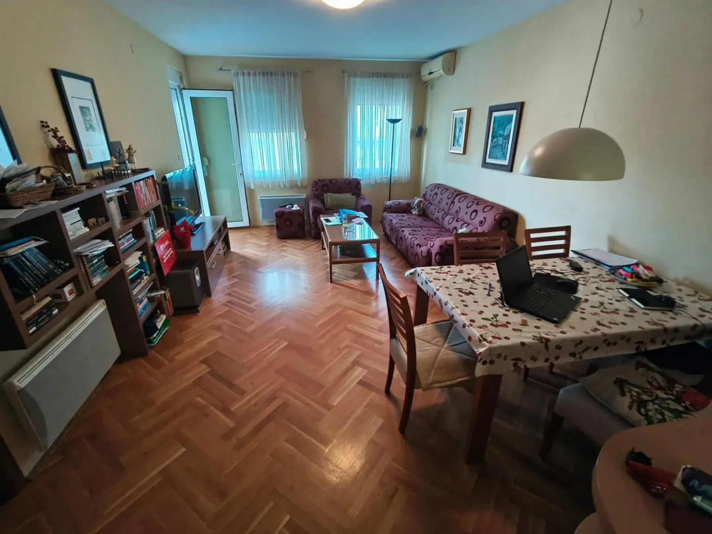 Dnevna soba sa garniturom, trpezarijskim stolom i policama za knjige.