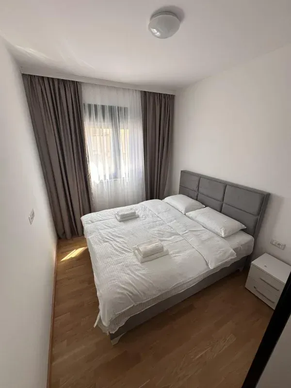 Svjetla spavaća soba sa bračnim krevetom, bijelom posteljinom i prozorom sa zavjesama.