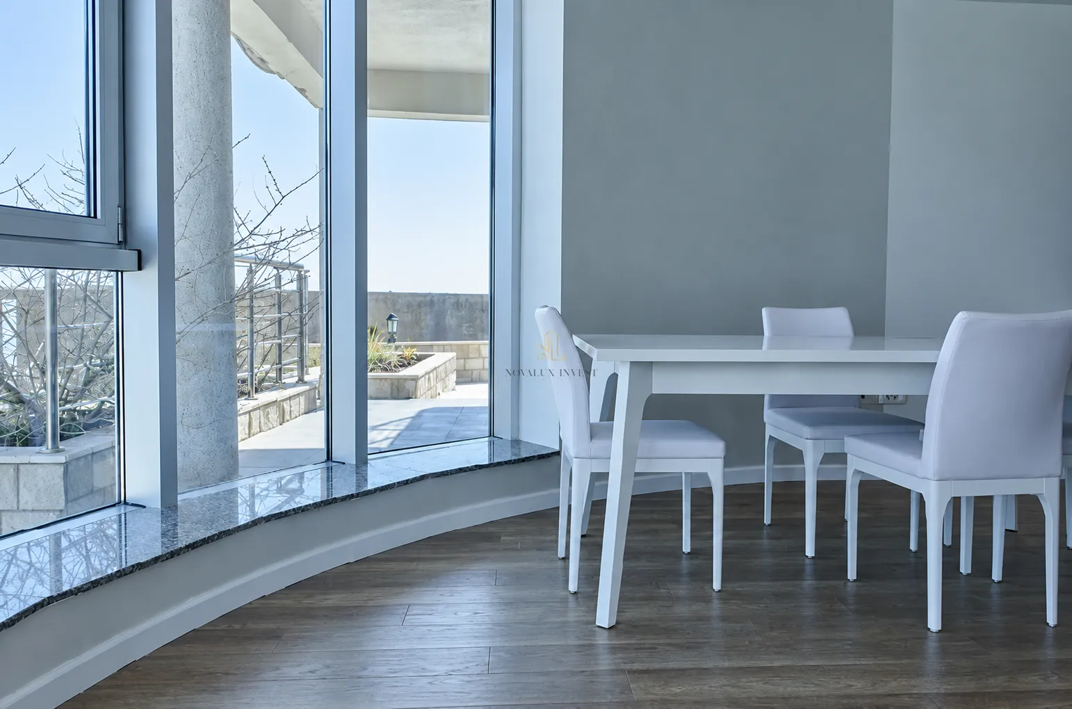 Dining area with a white table and chairs next to large windows with terrace access.