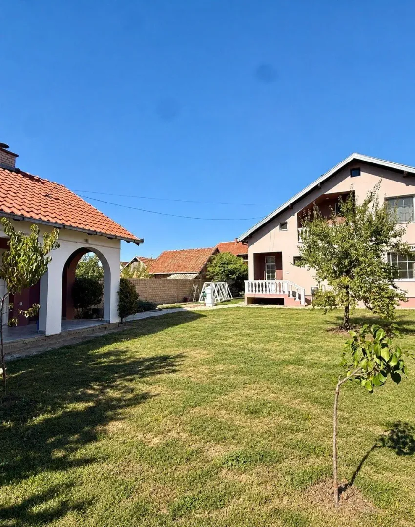 Dvorište sa travnjakom i dve kuće.