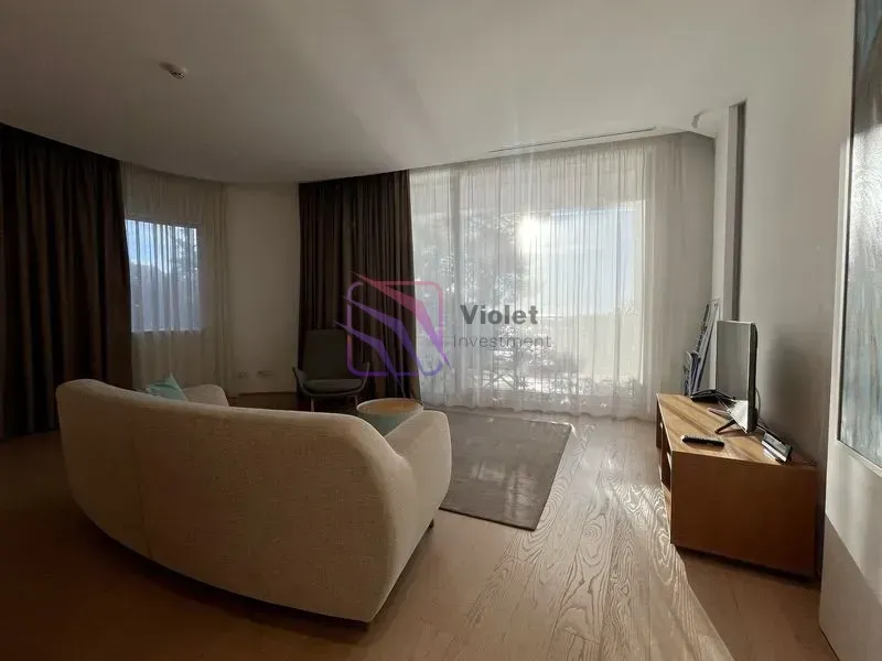 Dnevni boravak sa garniturom, TV komodom i velikim prozorima.