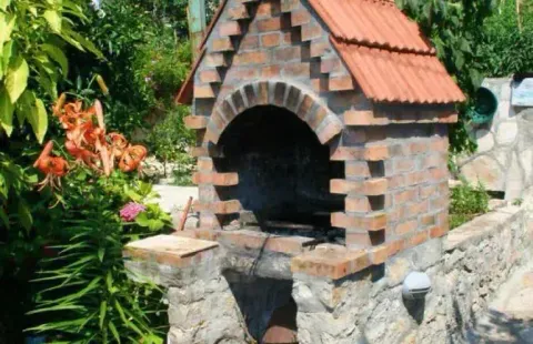 Zidani roštilj u dvorištu okružen zelenilom. - image 6