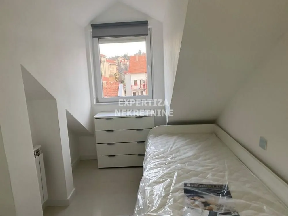 Attic bedroom with a bed and chest of drawers beneath the skylight.