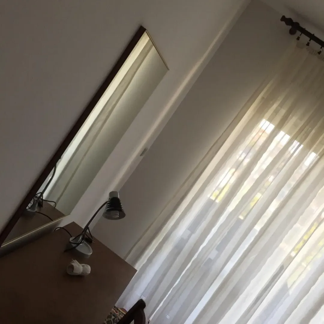 Detalj sobe sa stolom, ogledalom i prozorom sa svijetlim zavjesama.