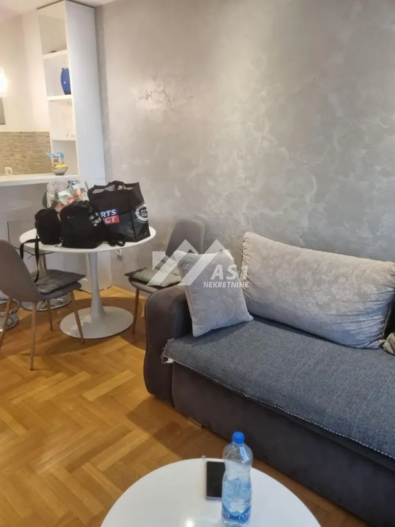 Dnevna soba sa ugaonom garniturom, trpezarijskim stolom i pogledom na kuhinju.