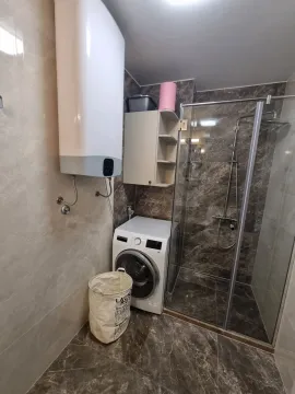 Modern bathroom with a glass shower, washing machine, and water heater. - image 8