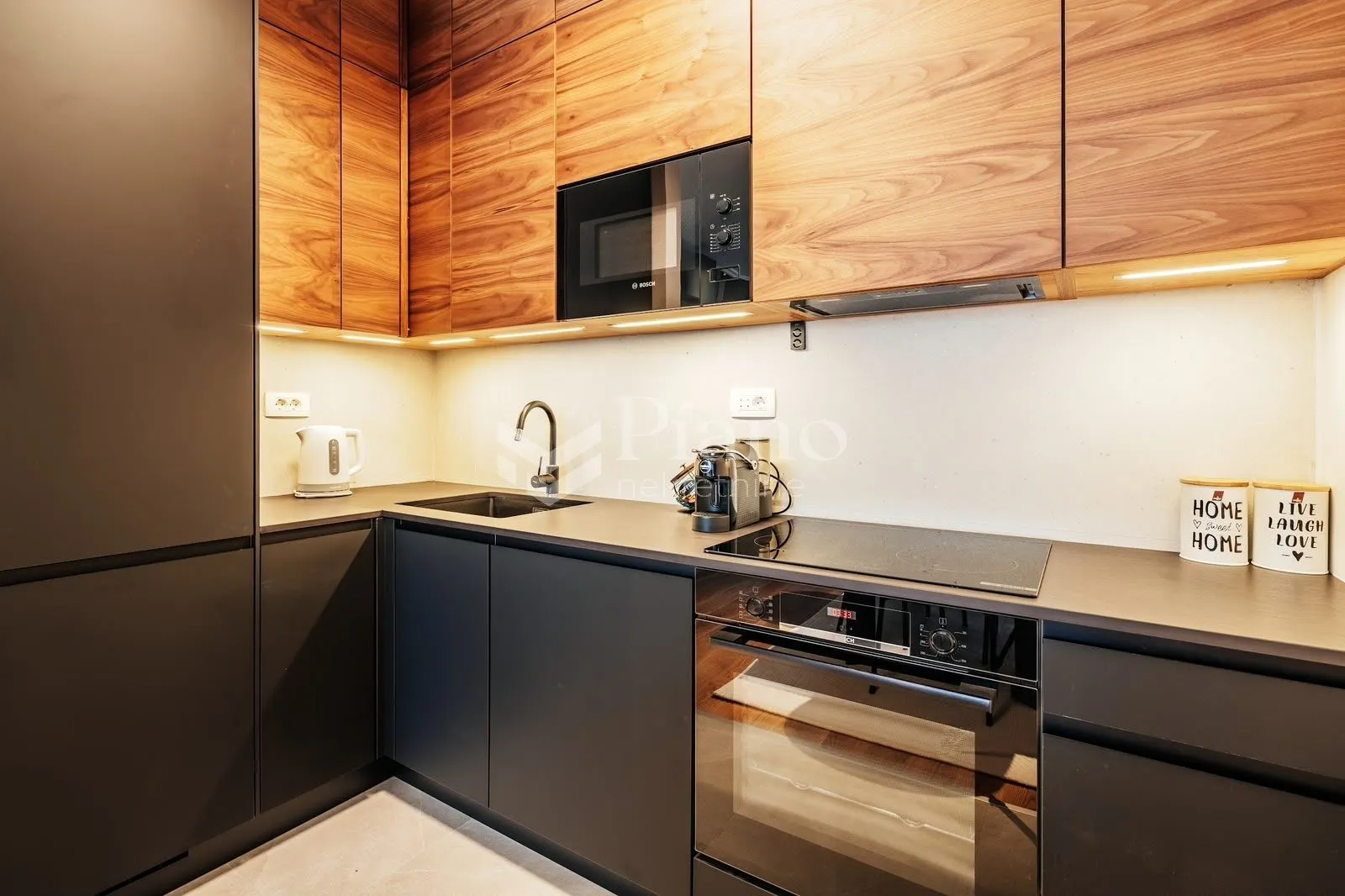 Modern kitchen with wooden upper cabinets, dark countertops, and integrated appliances.