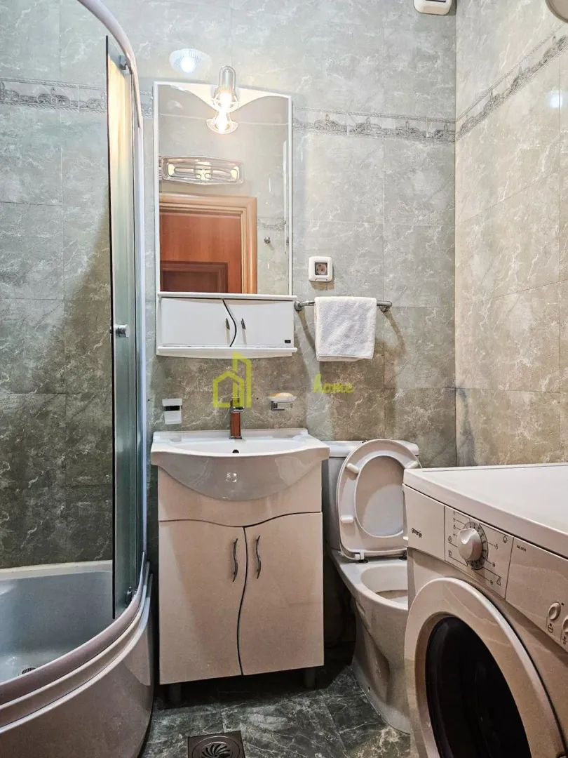 Compact bathroom with a shower cabin, washbasin, toilet, and washing machine.