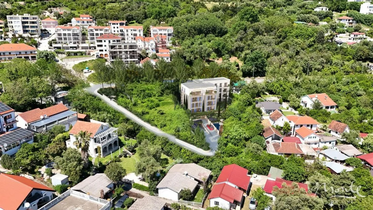 Pogled iz vazduha na novu stambenu zgradu okruženu zelenilom i porodičnim kućama.