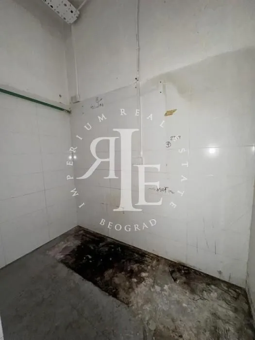 Empty room with white wall tiles and a rough floor.