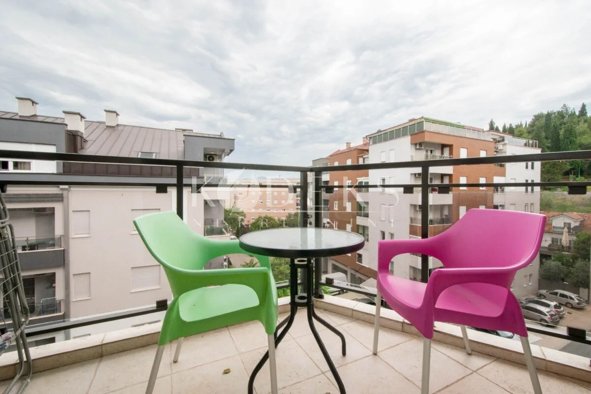 Small furnished balcony with a small table and two colorful chairs, overlooking the neighborhood.