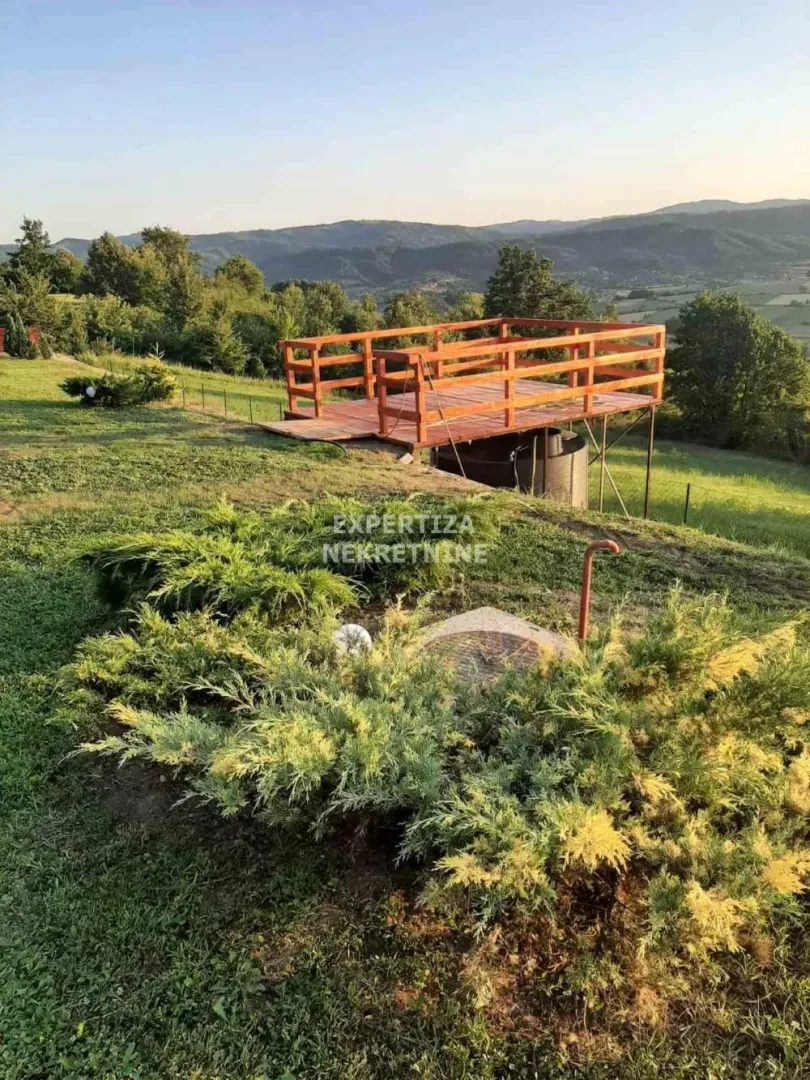 Pogled na drvenu terasu i travnato dvorište sa brdima u pozadini.