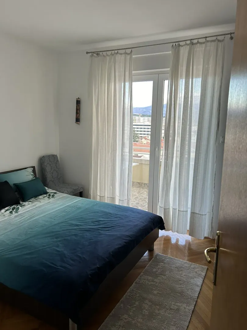 Svijetla spavaća soba sa bračnim krevetom i izlazom na balkon.