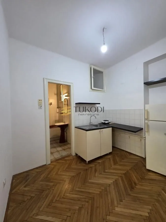 Small kitchen with parquet flooring and a view of the bathroom in the background.