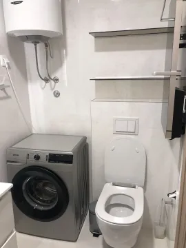 Bright bathroom with a washing machine and toilet. - image 12