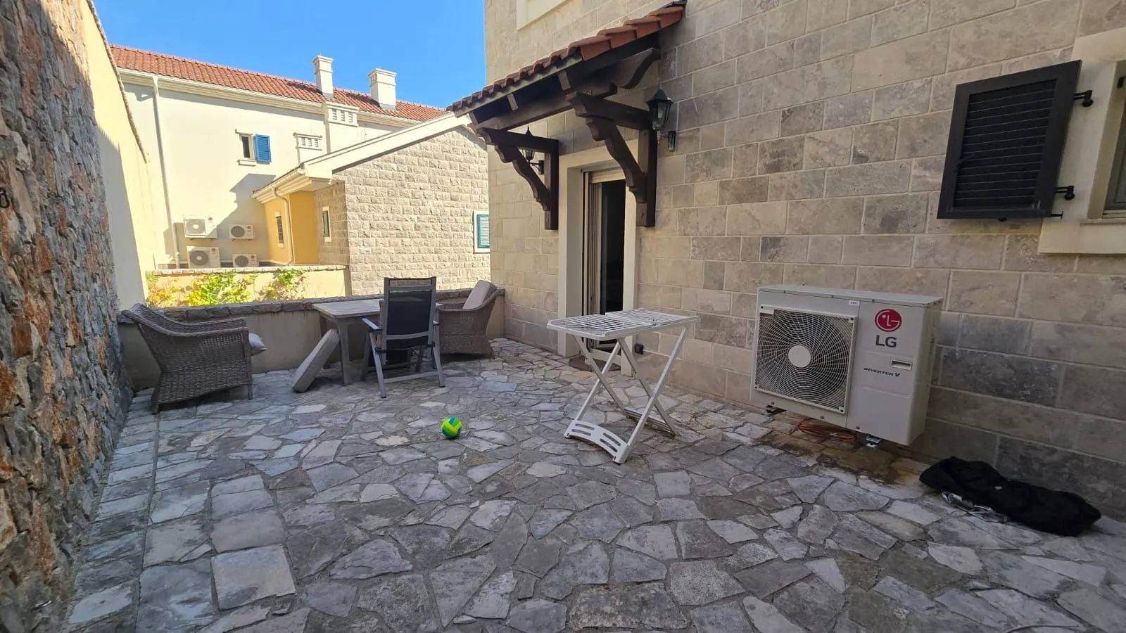 Popločano dvorište sa garniturom za sjedenje i klima uređajem.