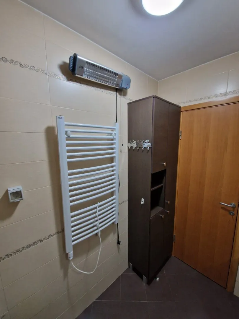 Dio kupatila sa sušačem peškira, grijalicom i visokim drvenim ormarićem.