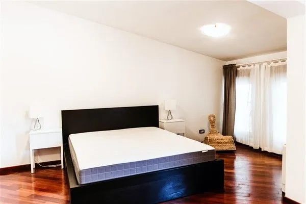 Bright bedroom with a dark double bed and wooden flooring.
