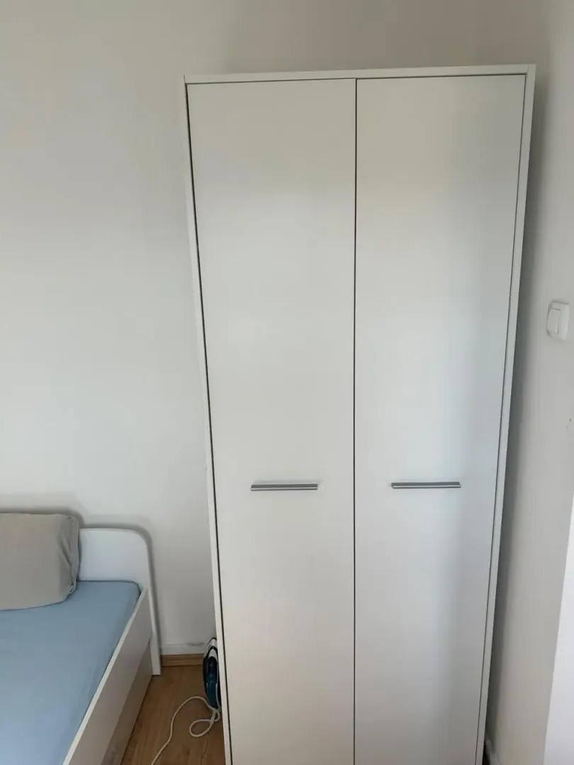 A white wardrobe in the bedroom next to the bed.