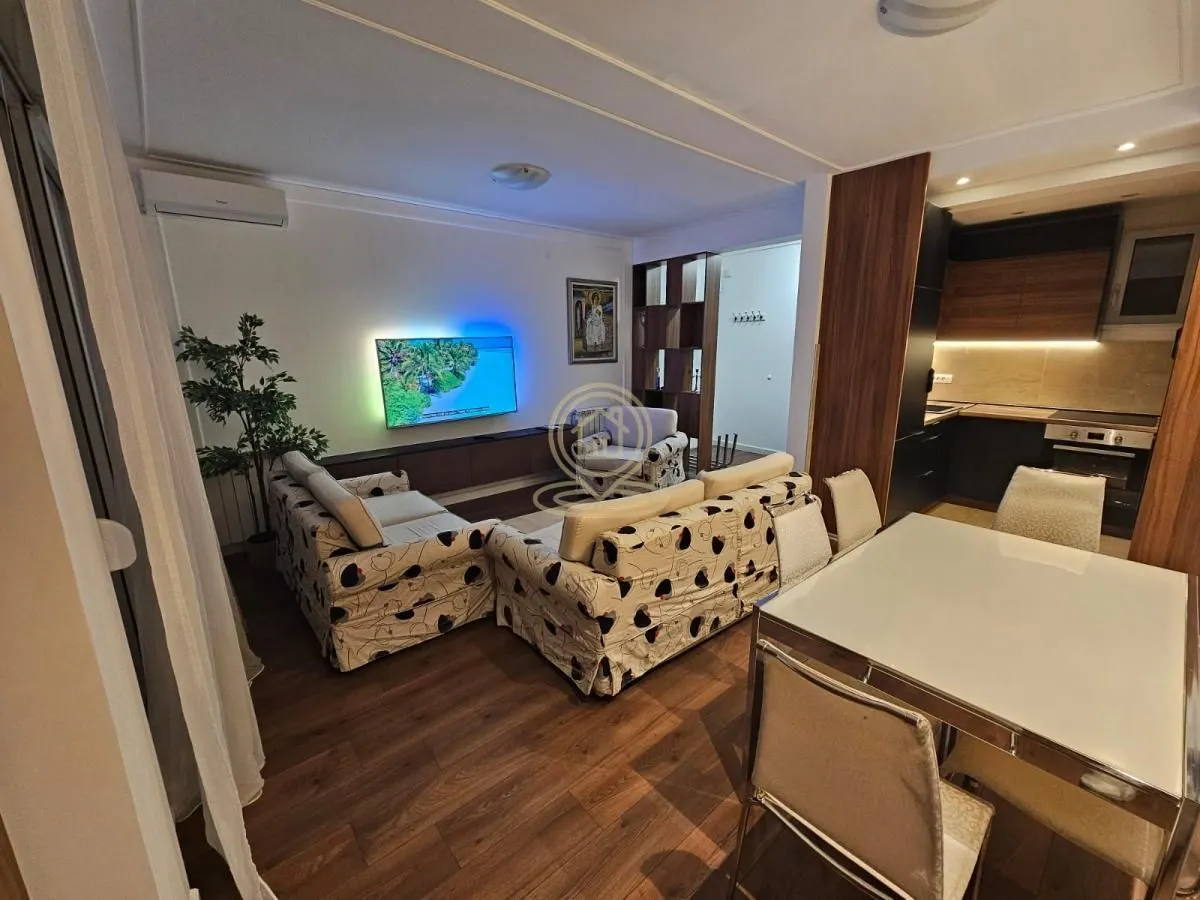 Living room with sofa, TV, dining area, and kitchen in the background.