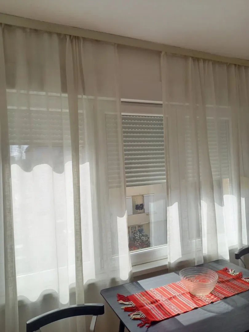 A window with white curtains and a dining table with a red runner.