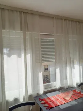 A window with white curtains and a dining table with a red runner. - image 12