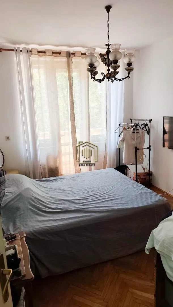 Furnished bedroom with a double bed, window, and chandelier.