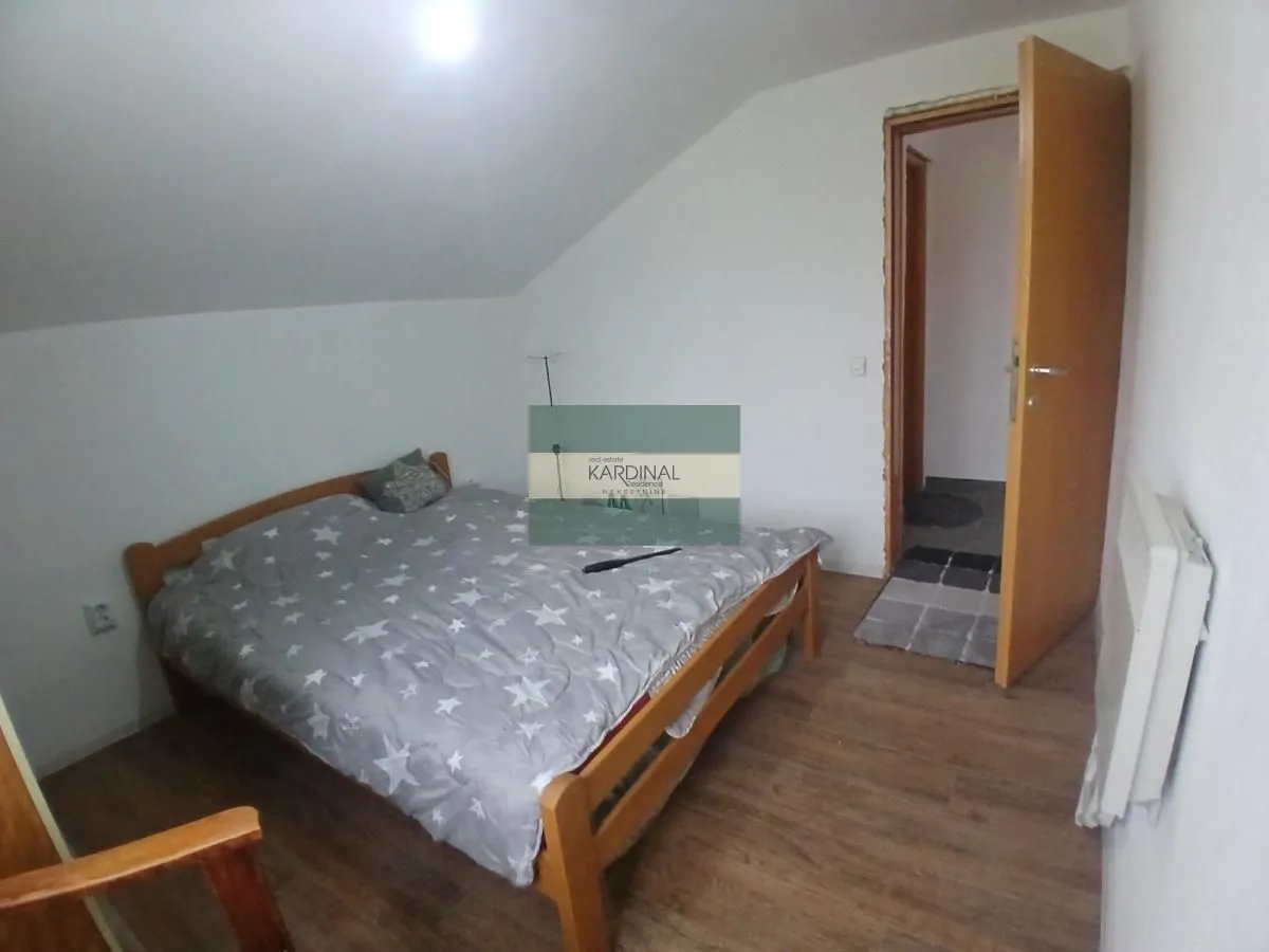 Manja spavaća soba sa drvenim krevetom i kosim plafonom.